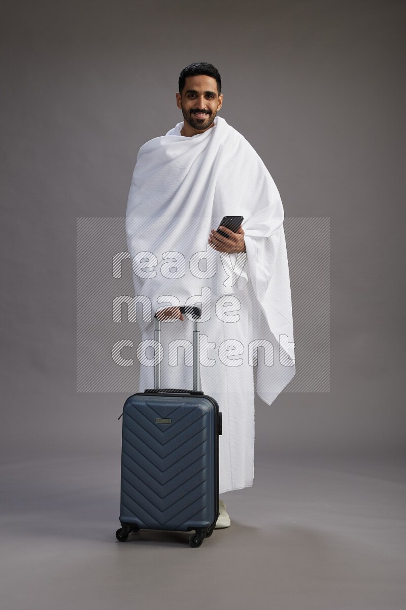 A man wearing Ehram Standing holding traveling bag on gray background