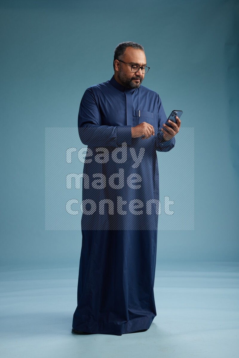 Saudi Man without shimag Standing texting on phone on blue background