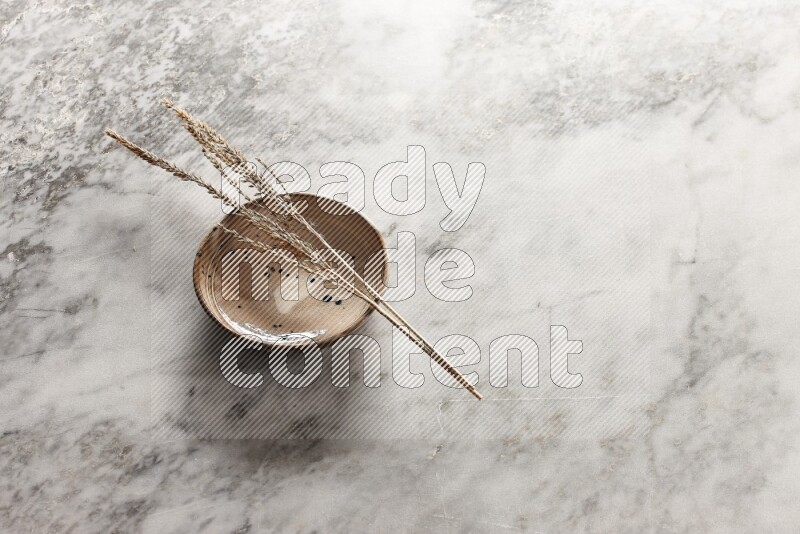 Wheat stalks on multicolored pottery bowl on grey marble background