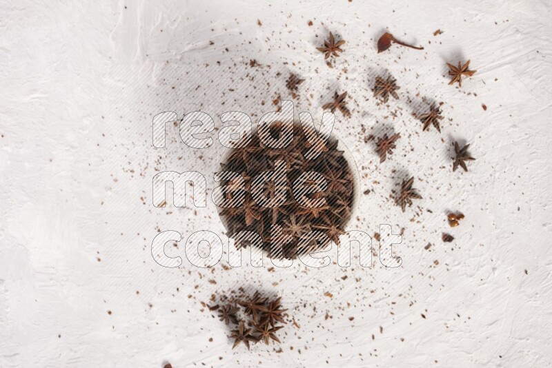 Star Anise in a white bowl and more of it sprinkled on white background