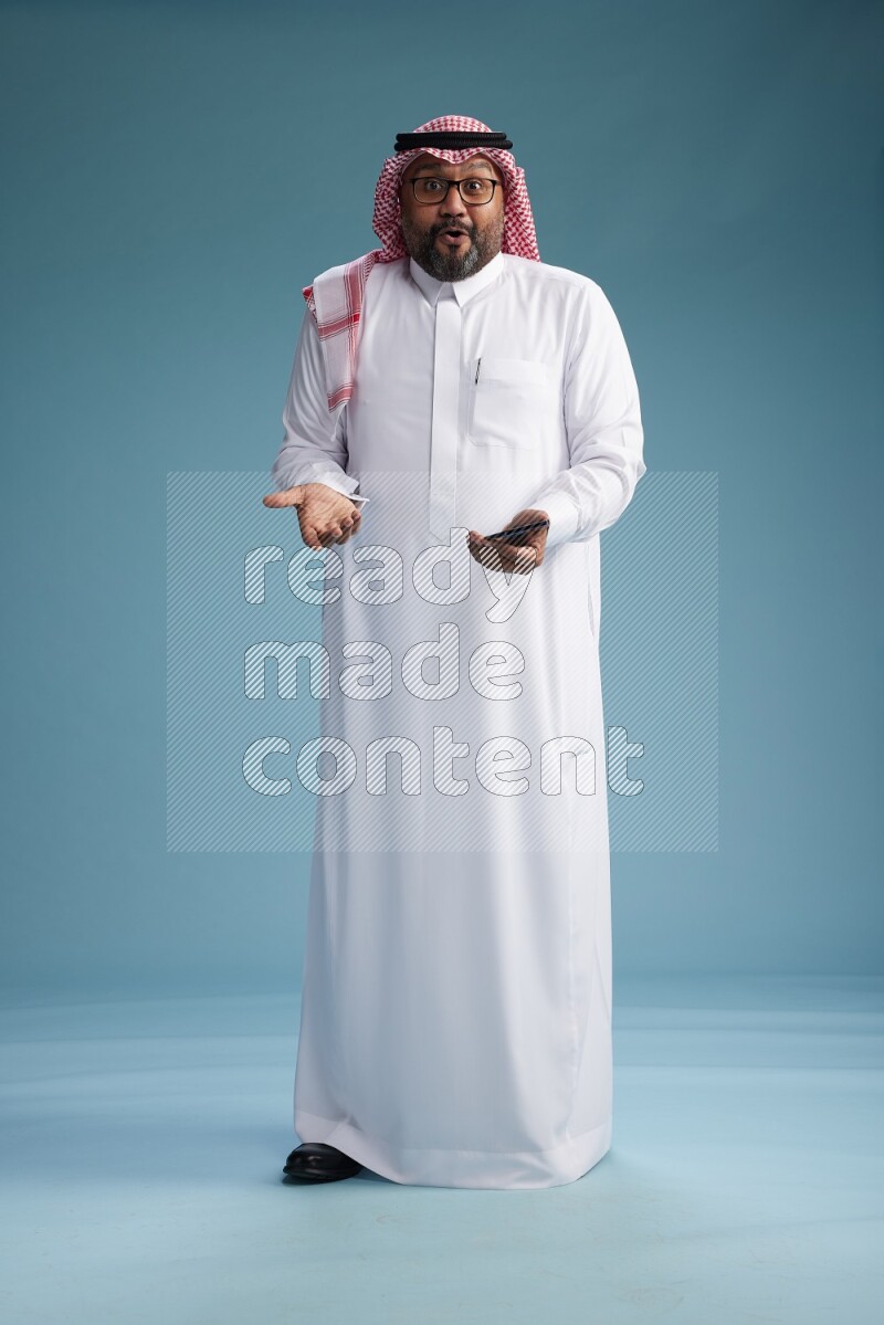 Saudi Man with shimag Standing texting on phone on blue background