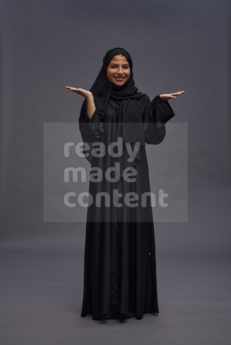 Saudi woman wearing Abaya standing interacting with the camera on gray background