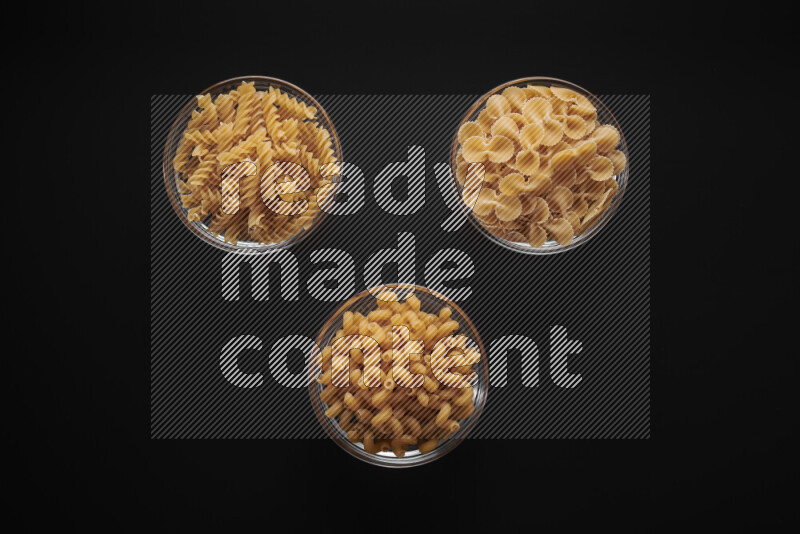 Different pasta types in glass bowls on black background