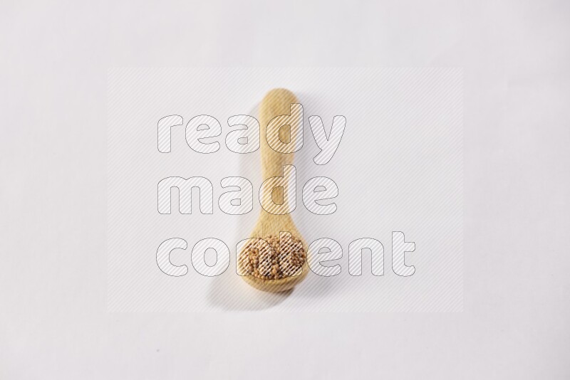 A wooden spoon full of mustard seeds on a white flooring