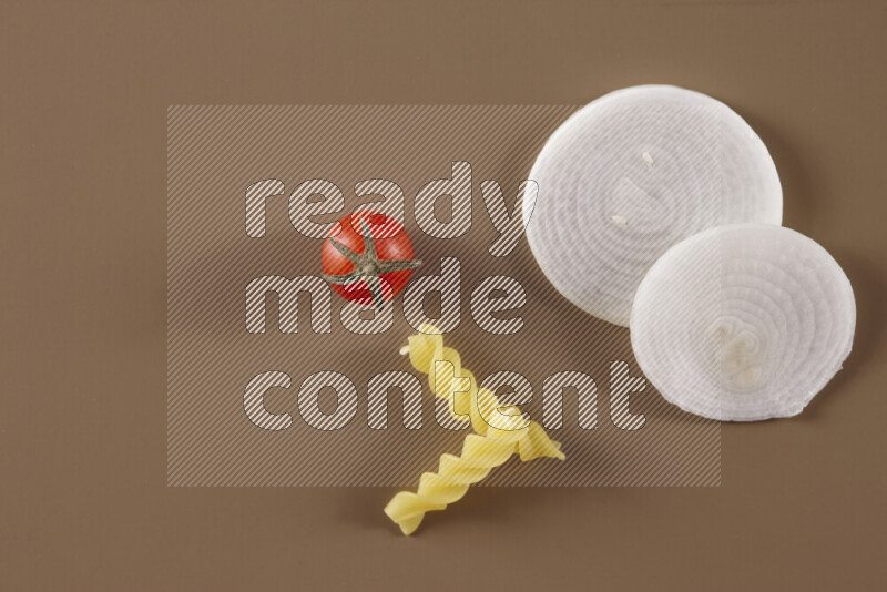 Raw pasta with different ingredients such as cherry tomatoes, garlic, onions, red chilis, black pepper, white pepper, bay laurel leaves, rosemary and cardamom on beige background