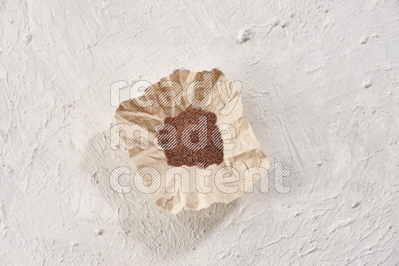 A crumpled piece of paper full of garden cress seeds on a textured white flooring
