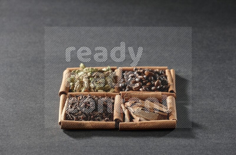 4 مربعات من عيدان القرفة ممتلئة بحبوب القهوة وقطع القرفة والقرنفل وحبوب الهيل على أرضية سوداء