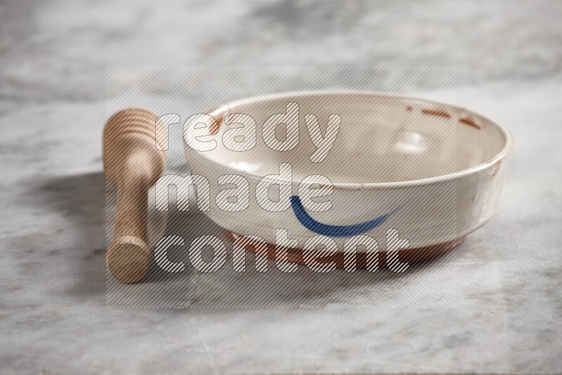 Multicolored pottery bowl with wooden honey dipper on the side on grey marble background
