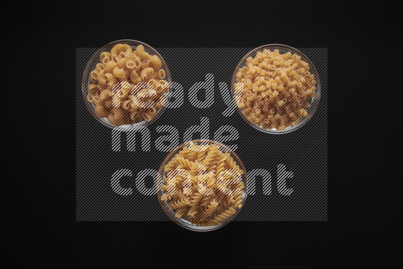 Different pasta types in glass bowls on black background