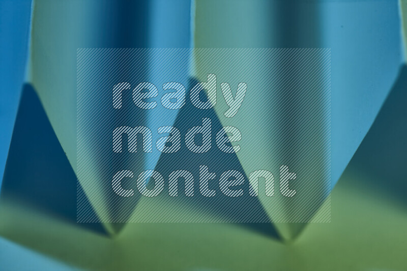 A close-up abstract image showing sharp geometric paper folds in green and blue gradients