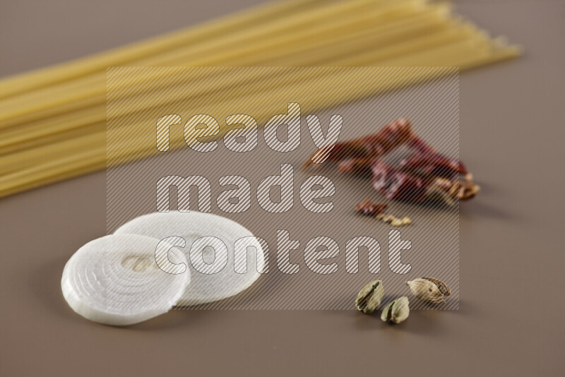 Raw pasta with different ingredients such as cherry tomatoes, garlic, onions, red chilis, black pepper, white pepper, bay laurel leaves, rosemary and cardamom on beige background