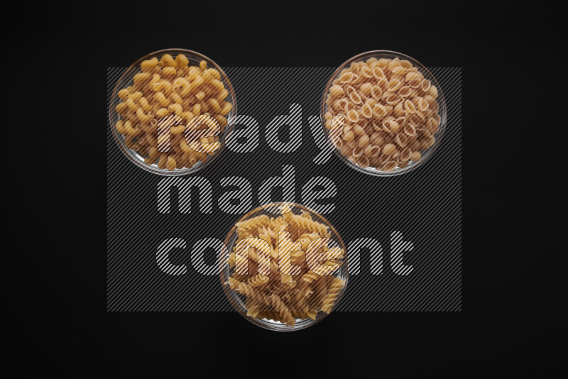 Different pasta types in glass bowls on black background