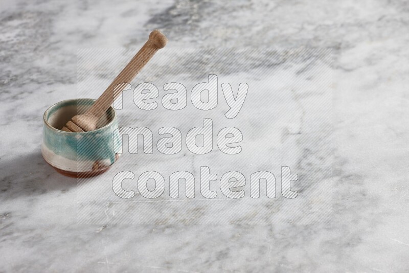 Multicolored pottery bowl with wooden honey dipper in it on grey marble background