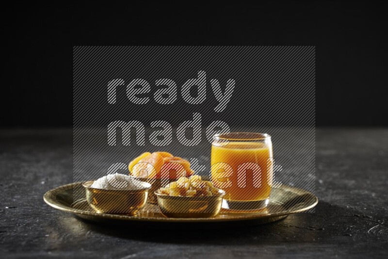 Dried fruits in metal bowls with qamar eldin on a tray in dark setup