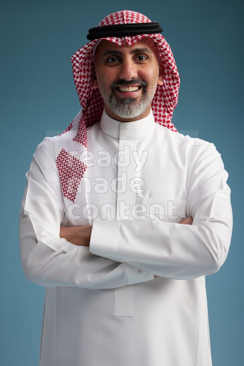Saudi man wearing thob and shomagh posing to the camera on blue background