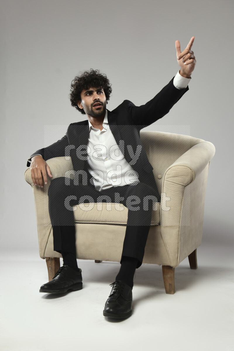A man wearing formal sitting on a chair making a hand gesture on white background