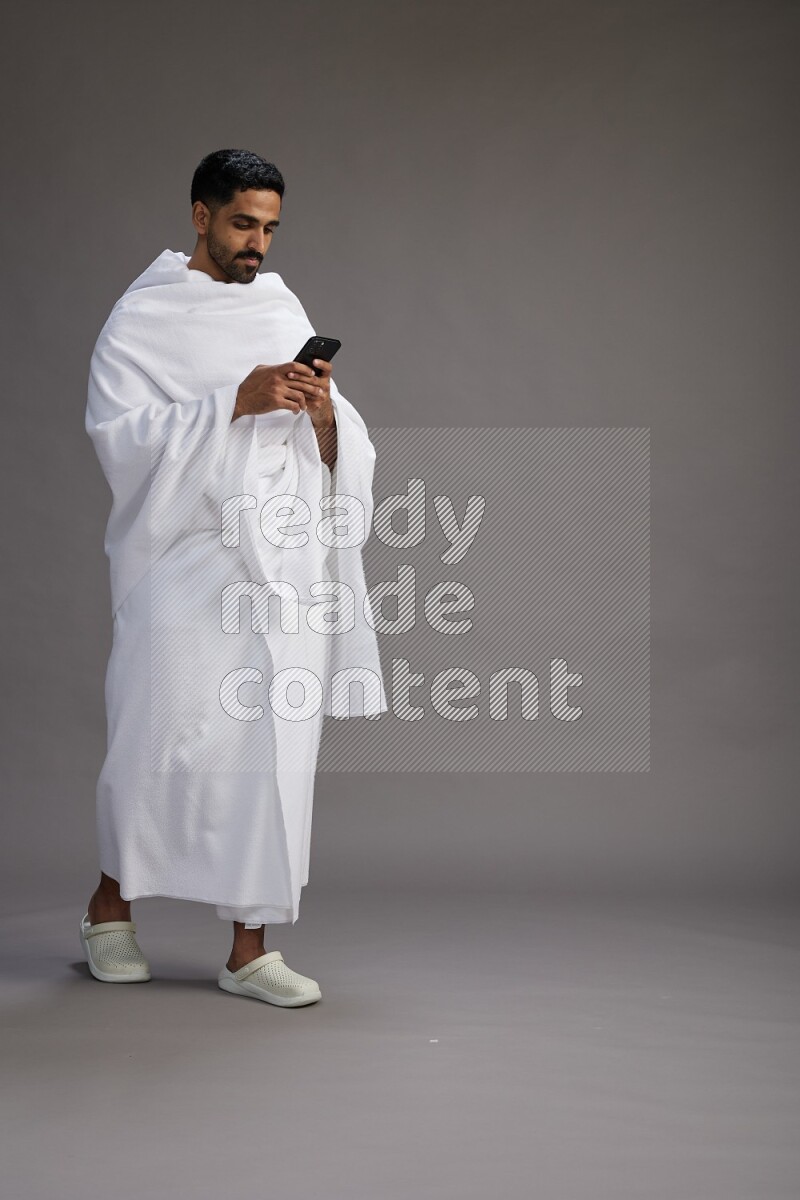 A man wearing Ehram Standing texting on phone on gray background