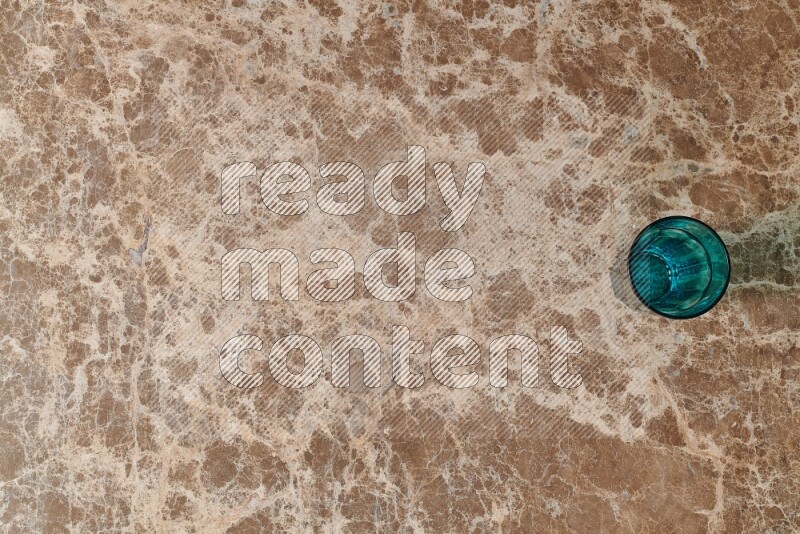 A turquoise glass cup on beige marble background