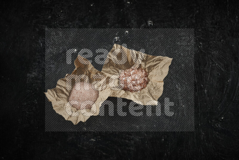 A crumpled piece of paper full of pink himalayan salt on black background