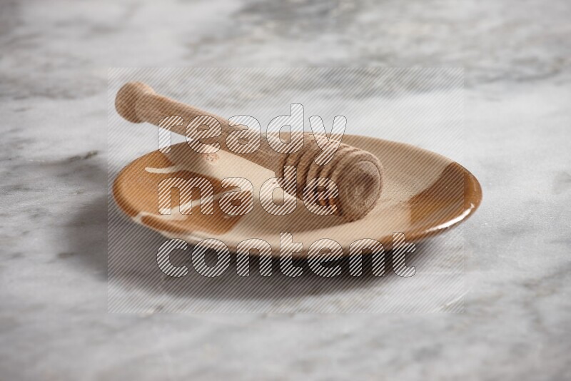Multicolored pottery plate with wooden honey dipper in it on grey marble background
