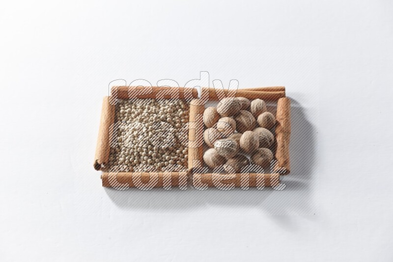 مربعان من أعواد القرفة ممتلئان بحبوب الفلفل الأبيض وجوزة الطيب علي خلفية بيضاء
