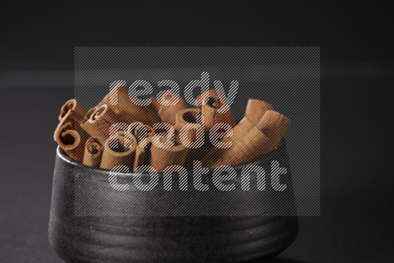 Cinnamon sticks in a black bowl on a black background in different angles