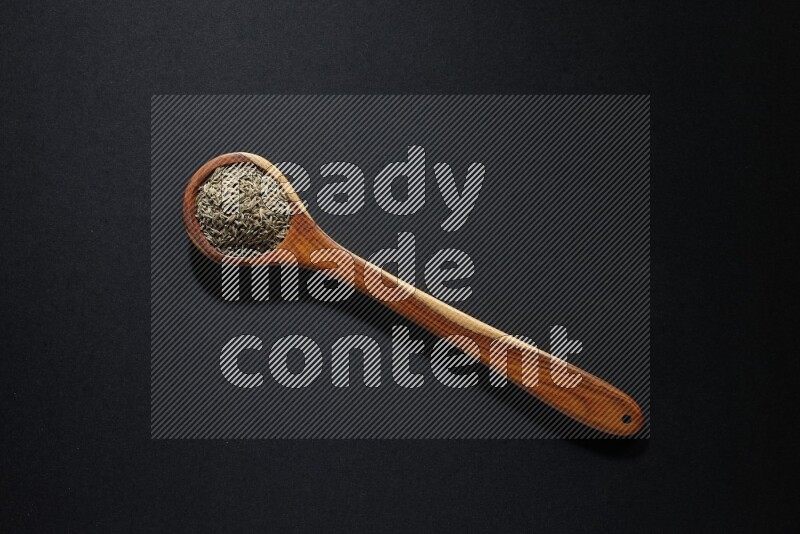 A wooden ladle full of cumin seeds on black flooring