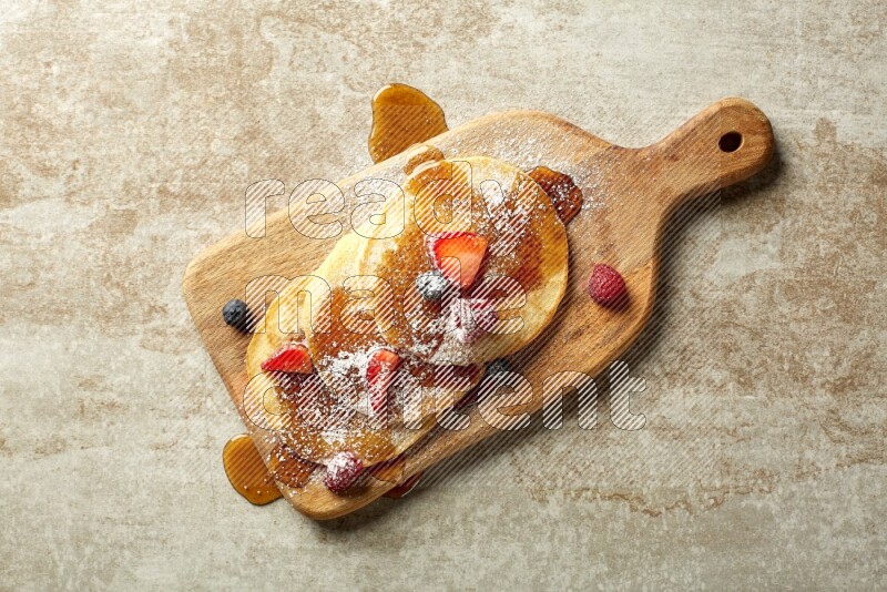 Three stacked mixed berries pancakes on a wooden board on beige background