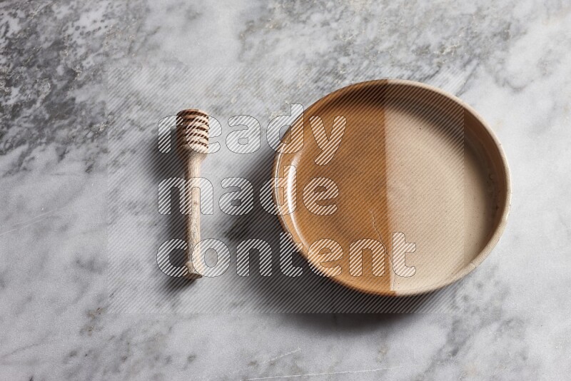 Multicolored pottery oven plate with wooden honey dipper on the side on grey marble background
