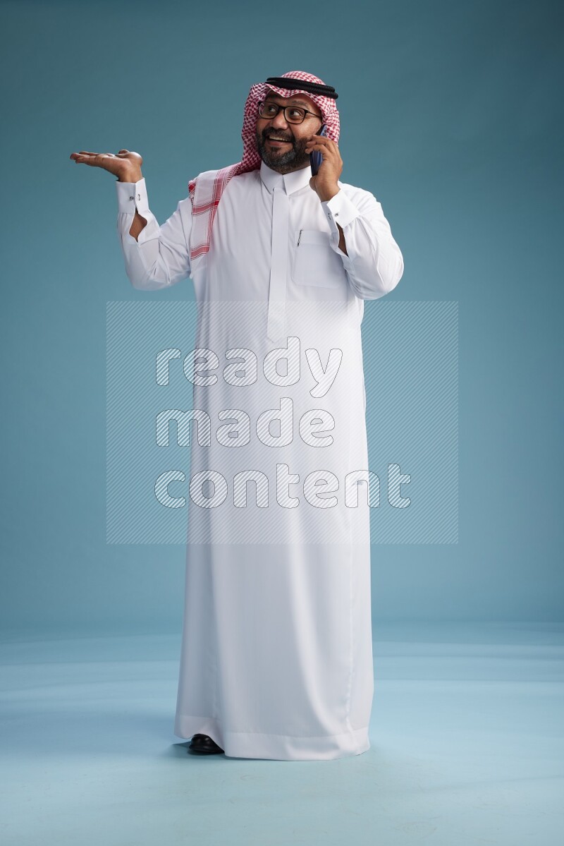 Saudi Man with shimag Standing talking on phone on blue background