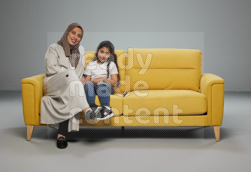 A girl with her mother sitting and interacting with the camera on gray background