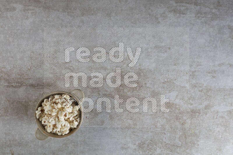 popcorn in a off-white handheld ceramic bowl on a grey textured countertop