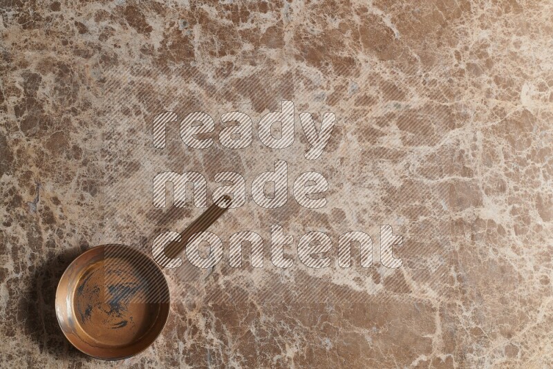 A small copper pan on beige marble background