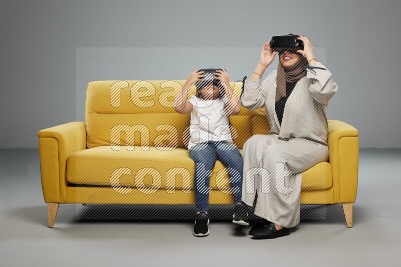 A girl and her mother sitting playing with VR on gray background