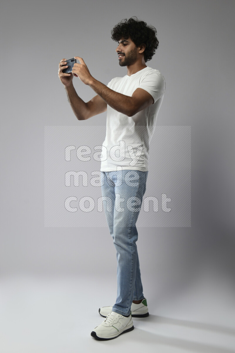 A man wearing casual standing and shooting with his phone on white background