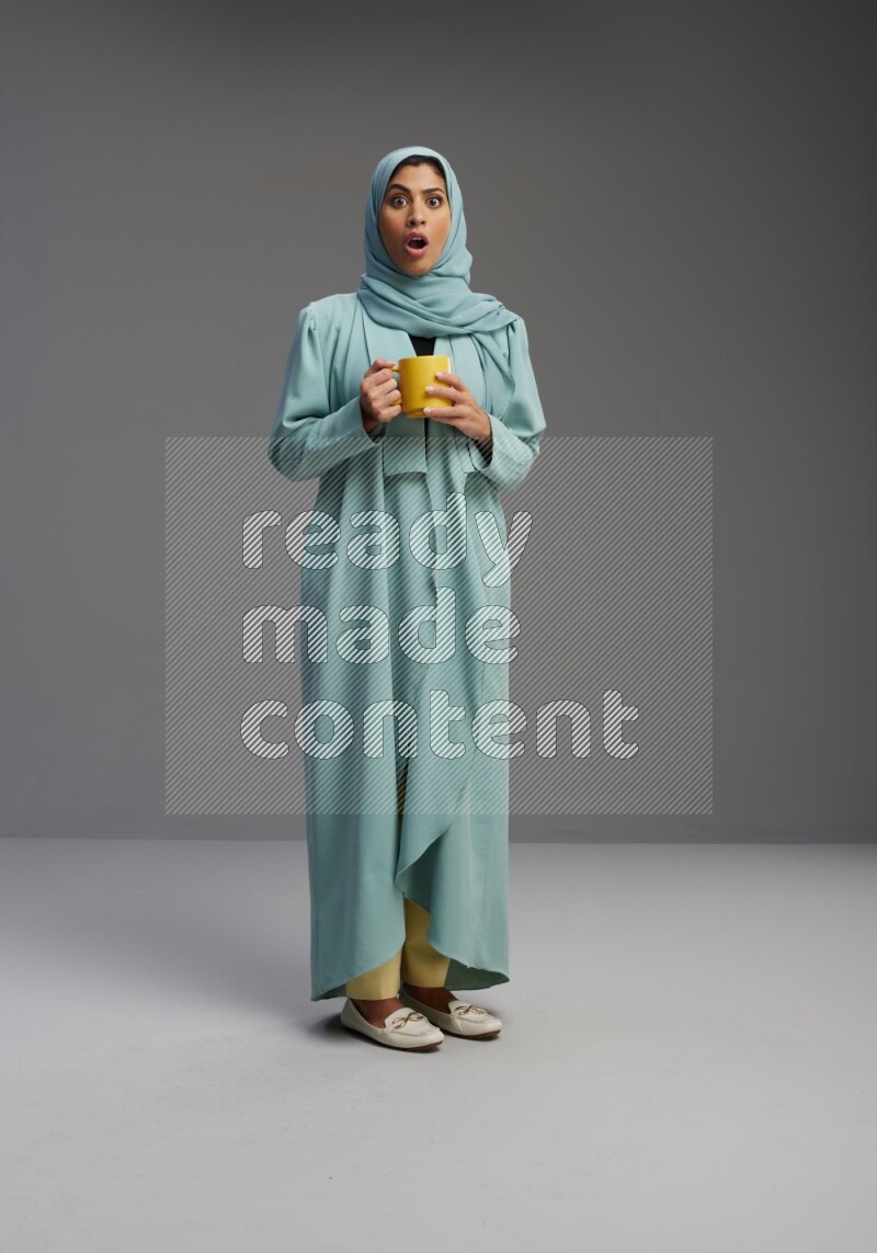 Saudi Woman wearing Abaya standing  holding a mug on Gray background