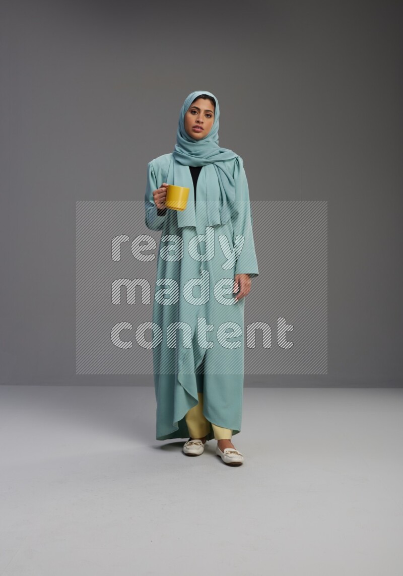 Saudi Woman wearing Abaya standing  holding a mug on Gray background