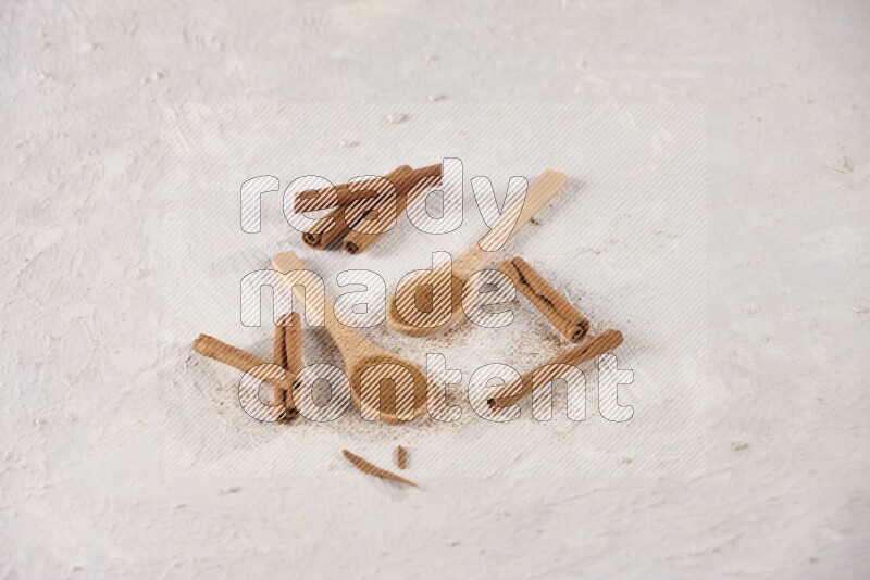 Two wooden spoons full of cinnamon powder with cinnamon sticks on white background