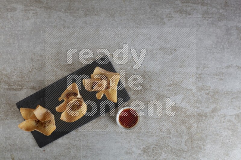 wonton cups with soy sauce ramkin on rectangle slate on grey textured counter top