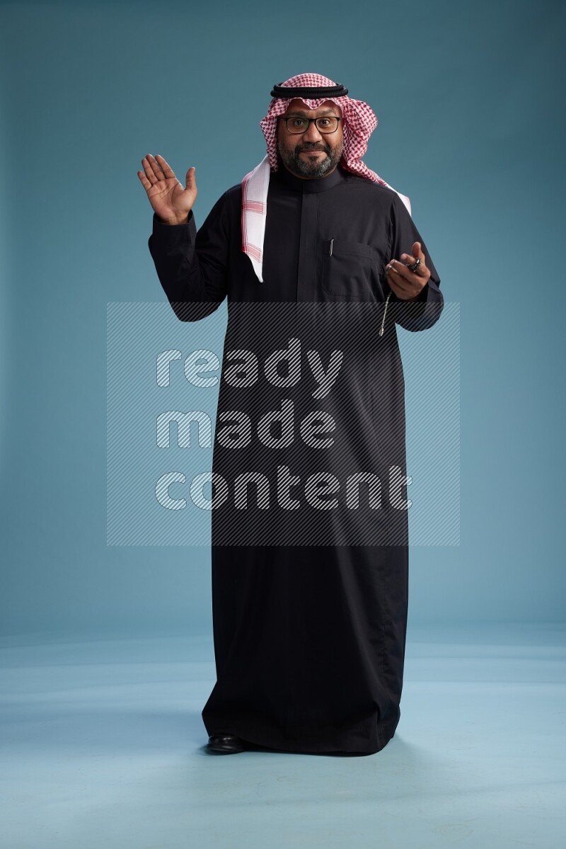 Saudi Man with shimag Standing Interacting with the camera on blue background