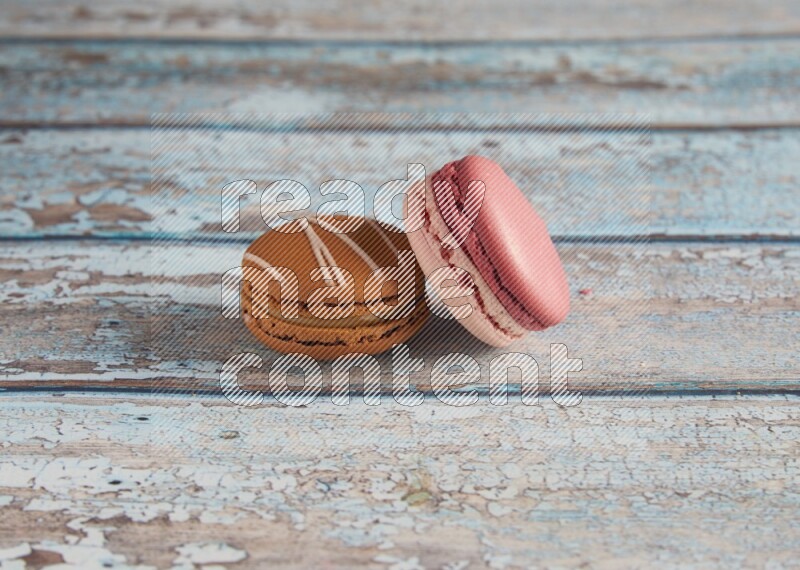 45º Shot of of two assorted Brown Irish Cream, and Pink Litchi Raspberry macarons on light blue background