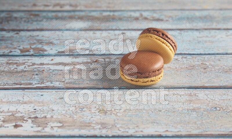 45º Shot of two Yellow and Brown Chai Latte macarons on light blue wooden background