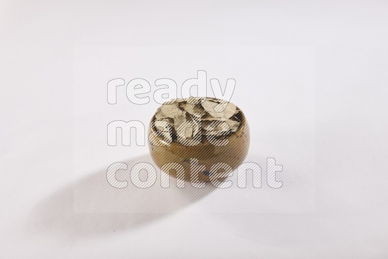 وعاء فخاري متعدد الألوان ممتلئ بأوراق الغار المجففة على أرضية بيضاء