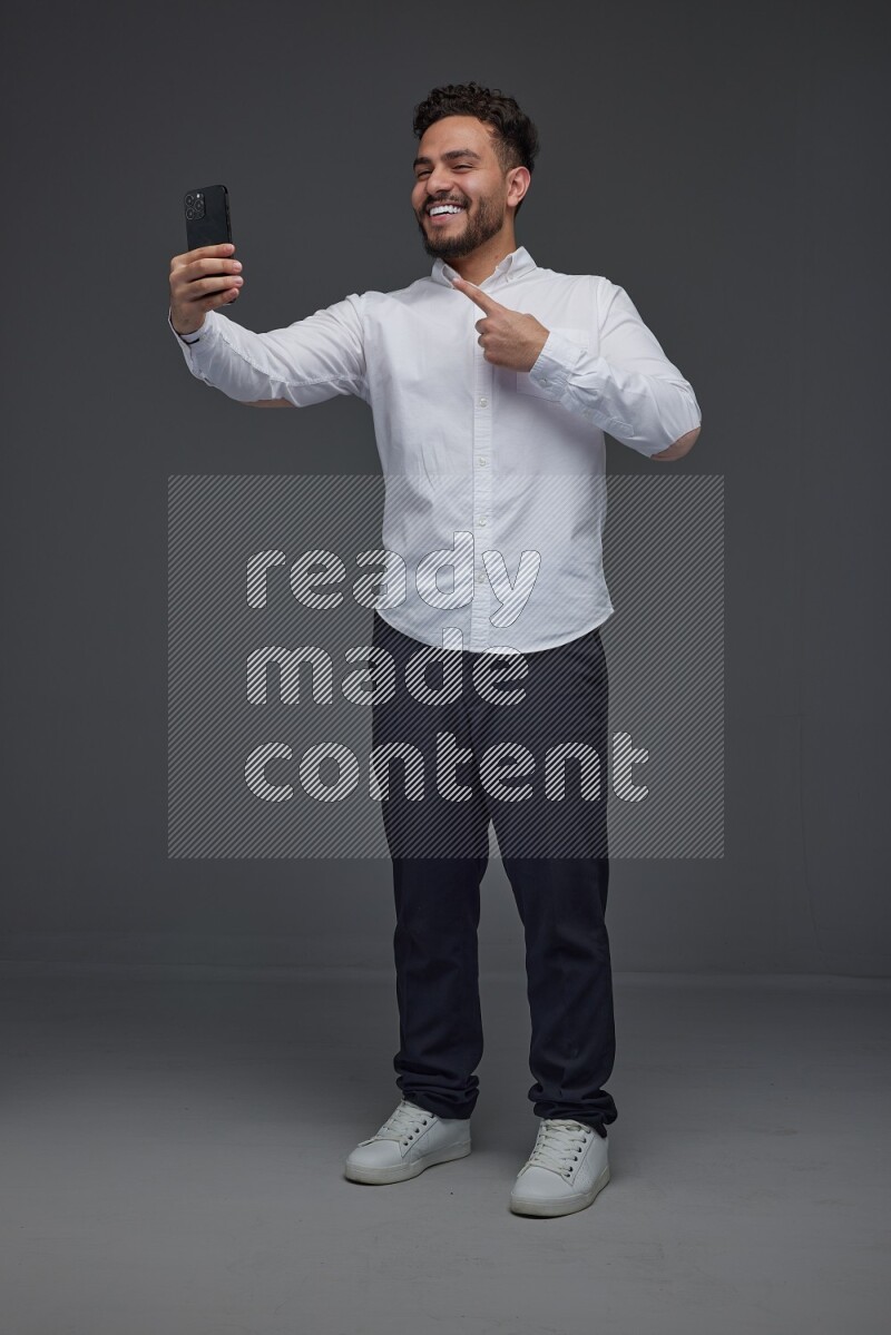 A man wearing smart casual and taking selfie with his phone eye level on a gray background