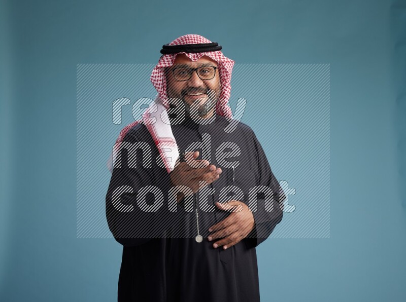 Saudi Man with shimag Standing Interacting with the camera on blue background