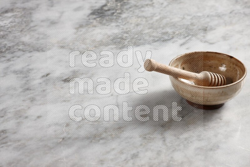 Beige pottery bowl with wooden honey dipper in it on grey marble background