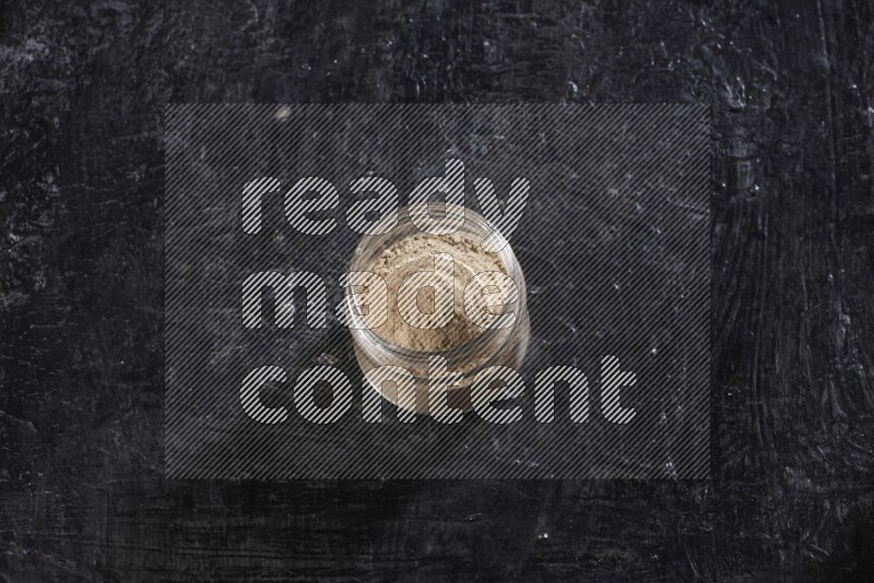 A glass jar full of garlic powder on a textured black flooring