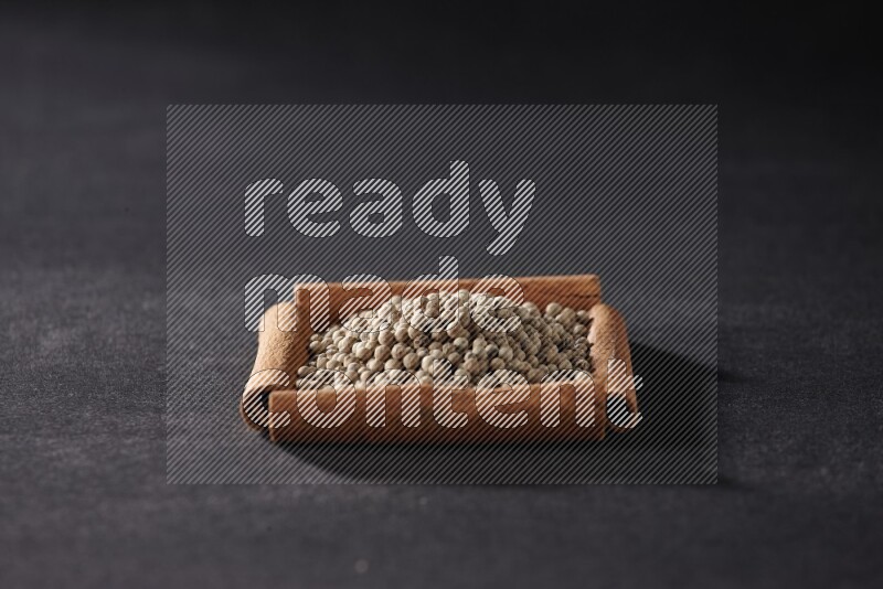 أربعة من أعواد القرفة مكونة شكل مربع بداخلها حبوب الفلفل الأبيض علي خلفية سوداء