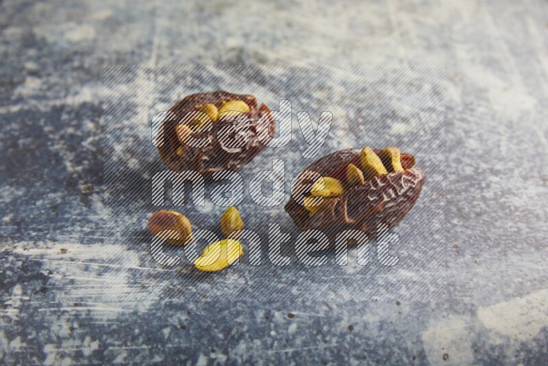 two pistachios stuffed madjoul dates on a rustic blue background