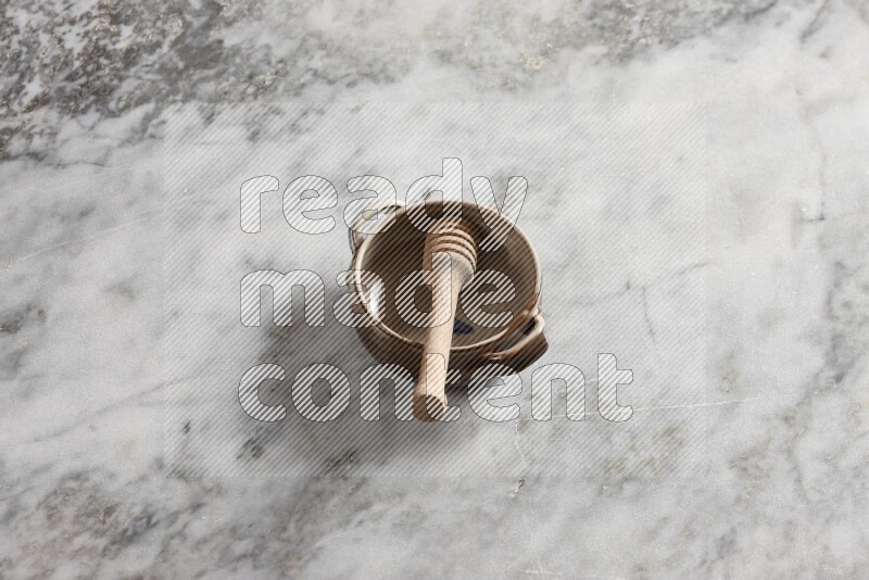 Multicolored pottery bowl with wooden honey dipper in it on grey marble background